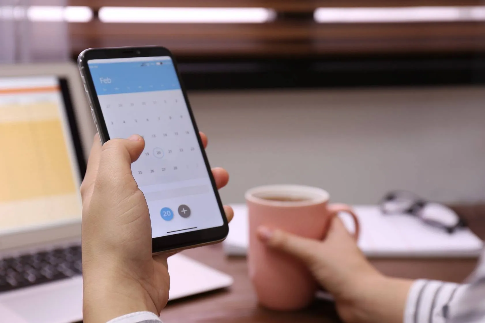 Frau hält Smartphone mit geöffnetem Kalender in der Hand